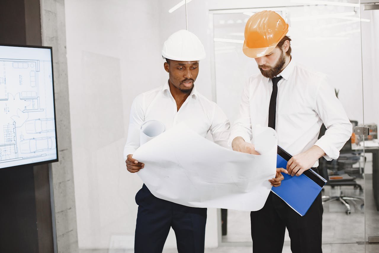 Two architects in hard hats review blueprints during a collaborative meeting in an office setting.